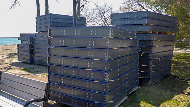 Construction materal piled on grass with a park bench on a sunny day.