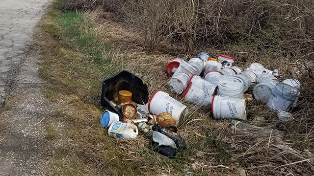 A pile of white cans and bins sit in a ditch beside a road