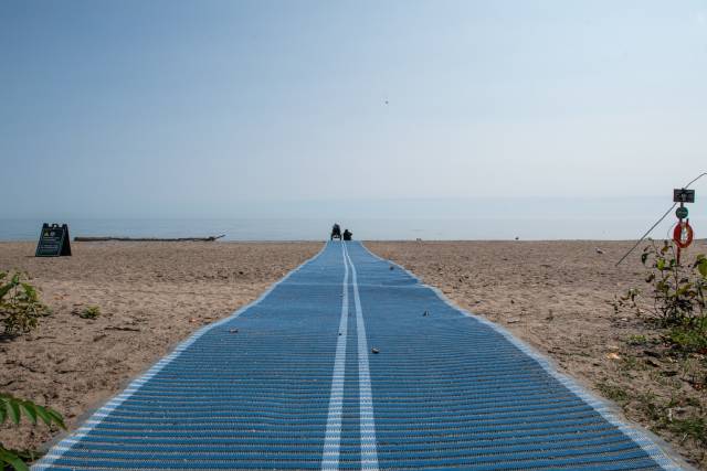 a beach scene with a blue mat leading towards the water,  /></p>
<figcaption class=