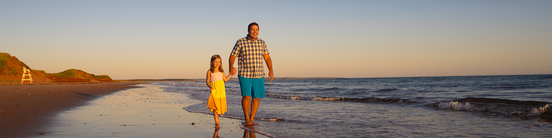 A man and a young girl walk along the beach in PEI National Park at sunset.