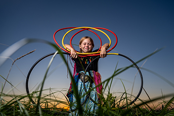 A young girl is holding multi coloured hoops in the grass.