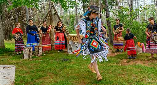 Mi'kmaw cultural heritage actors dancing in traditional clothing by a wigwam