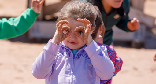 A young beach goer makes pretend glasses with their fingers.