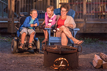 A family with accessibility needs enjoys a campfire in front of an oTENTik at Stanhope campground. Prince Edward Island National Park.
