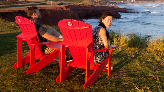 A couple sit on red chairs overlooking the water.