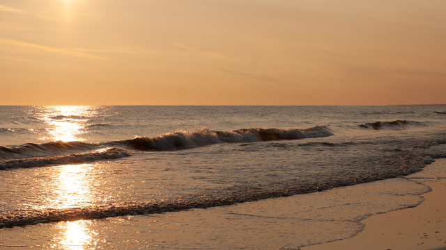 A golden sunrise over calm water with gentles waves