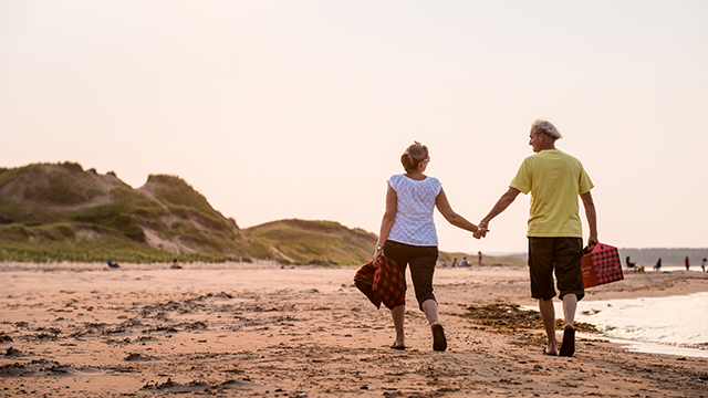 Two adults walk along the beach at sunset holding hands.
