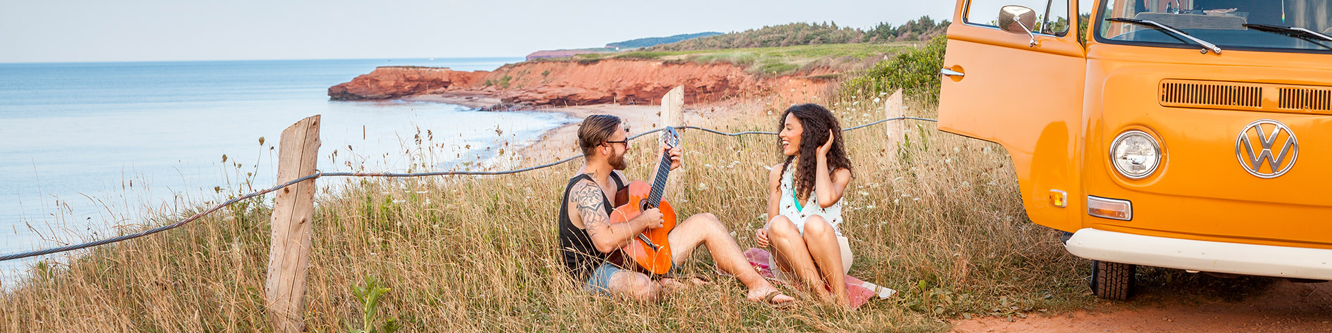 Un couple jouant de la guitare à côté d'un minibus rétro sur une côte près de Cavendish un jour d'été. Parc national de l’Île-du-Prince-Édouard