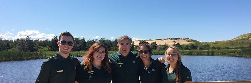 A group of five Parks Canada staff in uniform stand smiling on the Greenwich floating boardwalk in PEI National Park.