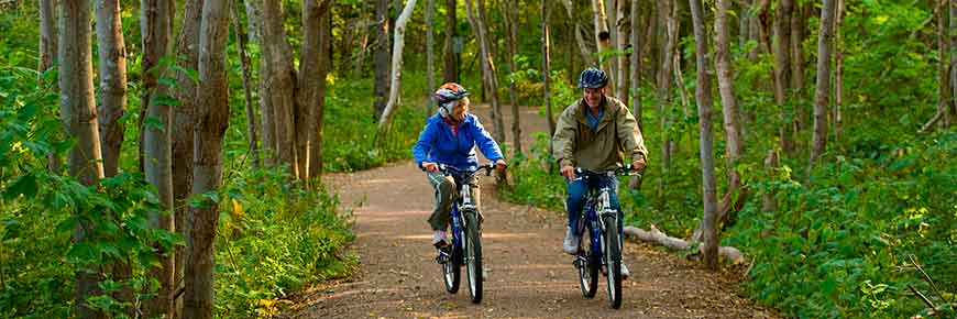 Two cyclists bike along a trail in a wooded area of PEI National Park.