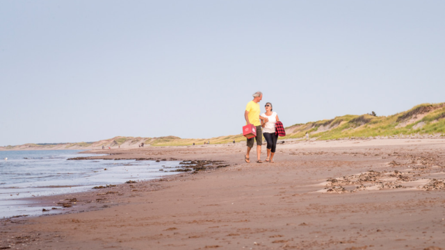 Un couple marche le long de la plage Brackley, prêt à s’offrir le pique-nique idéal. Parc national de l’Île-du-Prince-Édouard. 