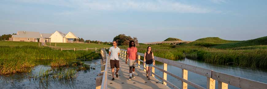Three youth walk on the Cavendish Dunelands Trail, with Cavendish Beach and facilities in the background. 