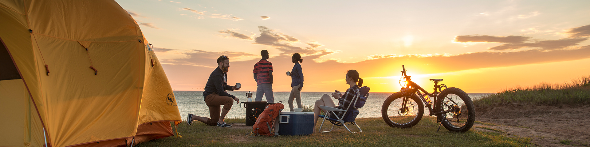 Un groupe d’amis profite du lever du soleil à l’extérieur de sa tente au terrain de camping de Cavendish. Parc national de l’Île-du-Prince-Édouard. 