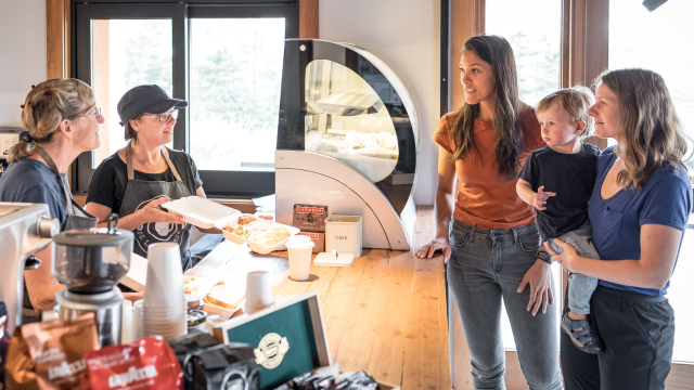 Deux employés d'un café servent un plat à des visiteuses. 