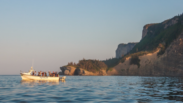 A ship is parked in a cove with the cliffs of Cap Bon-Ami in the background.