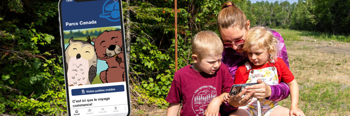 Une mère et ses denx enfants regardent un smartphone sur un banc en nature.