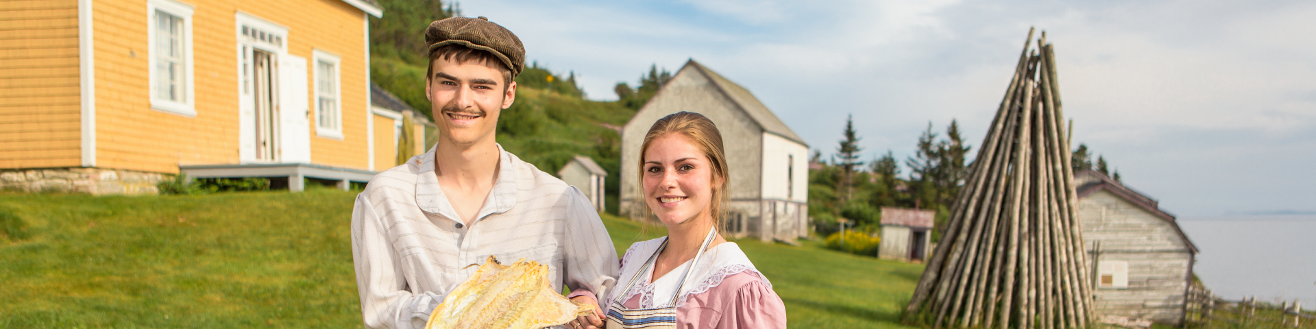 Two employees in period costume present a dried and salted cod on the Anse-Blanchette site. 