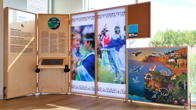 Modular reception and interpretation space with photos of traditionnal dancers and a mural representing Forillon National Park.