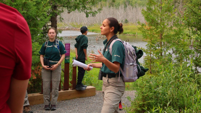 A Parks Canada employee is speaking to a group of people near a beaver pond.