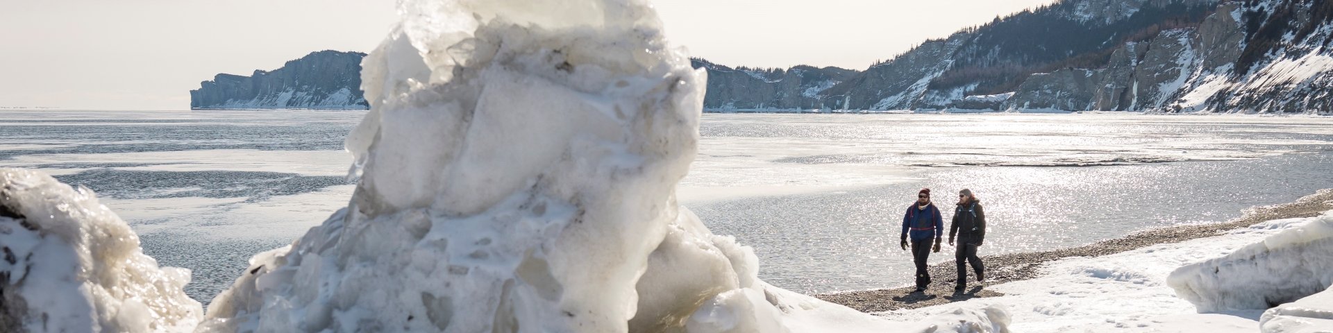 Two visitors walk on a beach in winter with cliffs in the background