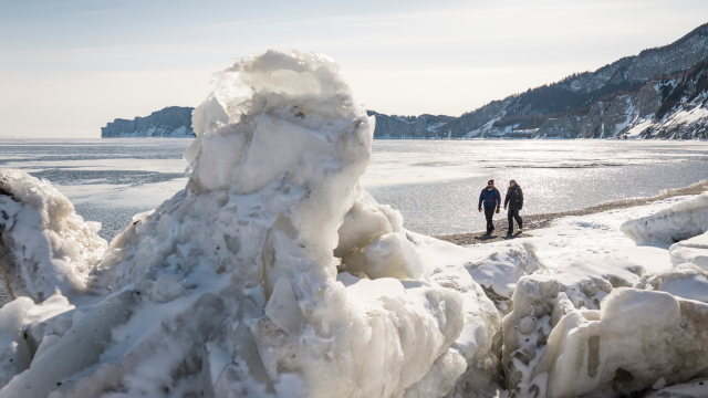 Deux hommes parchent sur la plage de Cap-des-Rosiers en hiver avec les falaises du Cap-Bon-Ami en arrière-plan. 