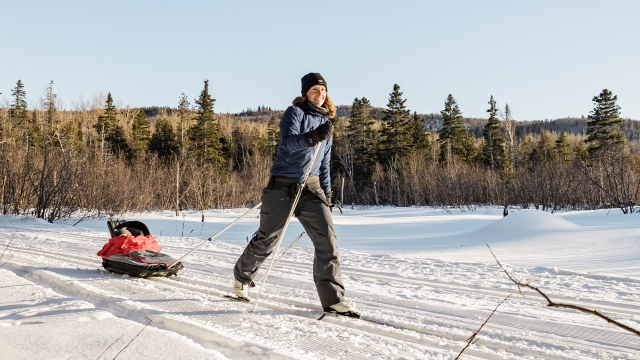 Une skieuse de fond tire un traineau pour bébé. 