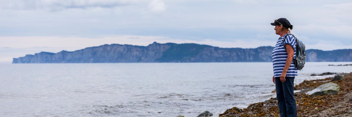 Une visiteuse, debout, regarde vers la mer sur la plage de Cap-des-Rosiers. 
