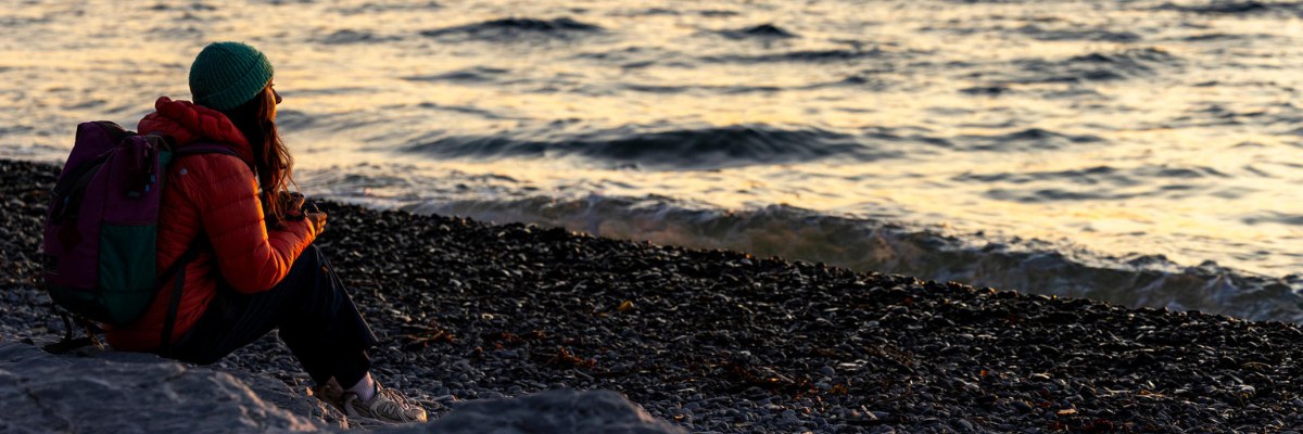 Une visiteuse admire le lever du soleil d'une plage de galets.