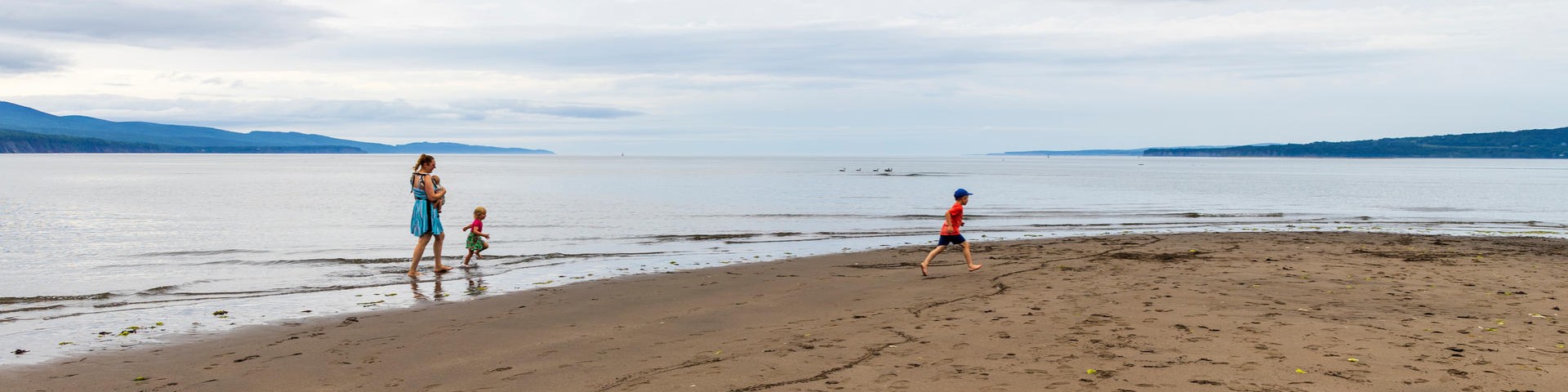 Trois personnes marchent sur un banc de sable près de la plage.
