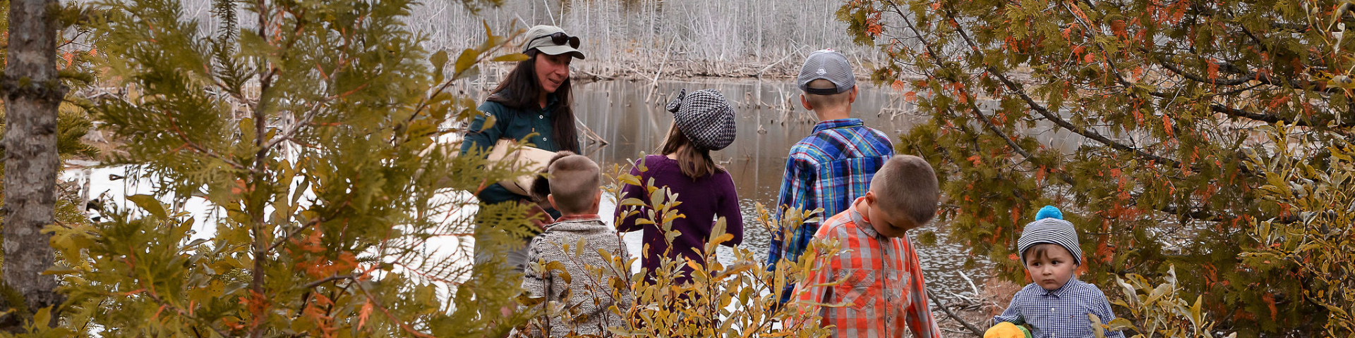 An interpreter speaks to a group of children nearby a pond.