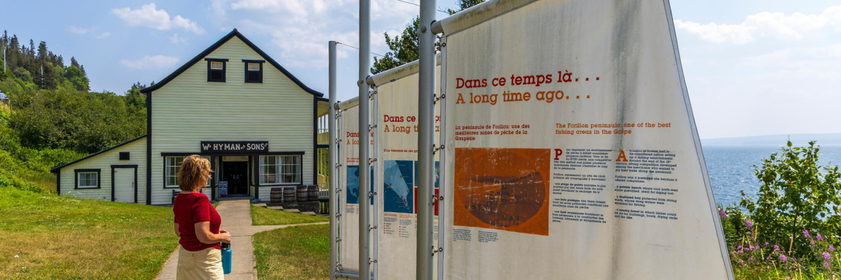 A woman is reading information about fishing on a banner outside a general store.