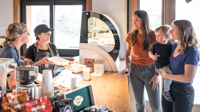 Two employees show a plate to two customers holding a baby, one is holding a baby. 