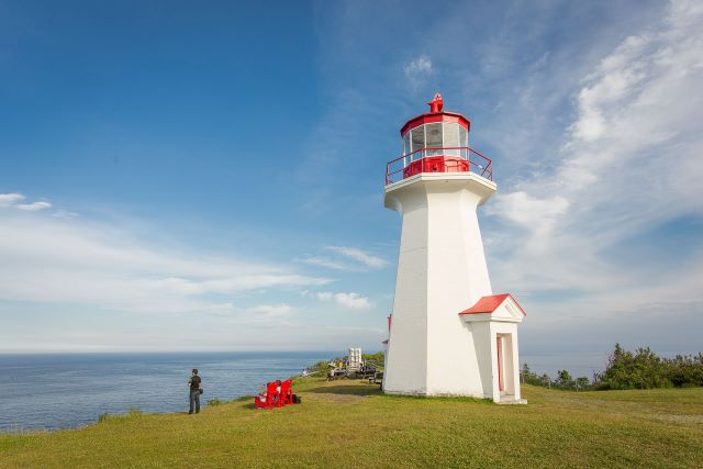 Un visiteur regarde la mer au pieds d'un phare. 