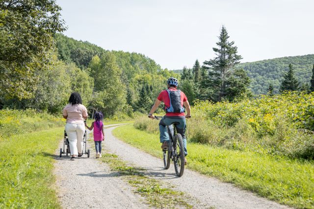 A visitor on a mountain bike is about to overtake a family of hikers on a multi-use trail. 