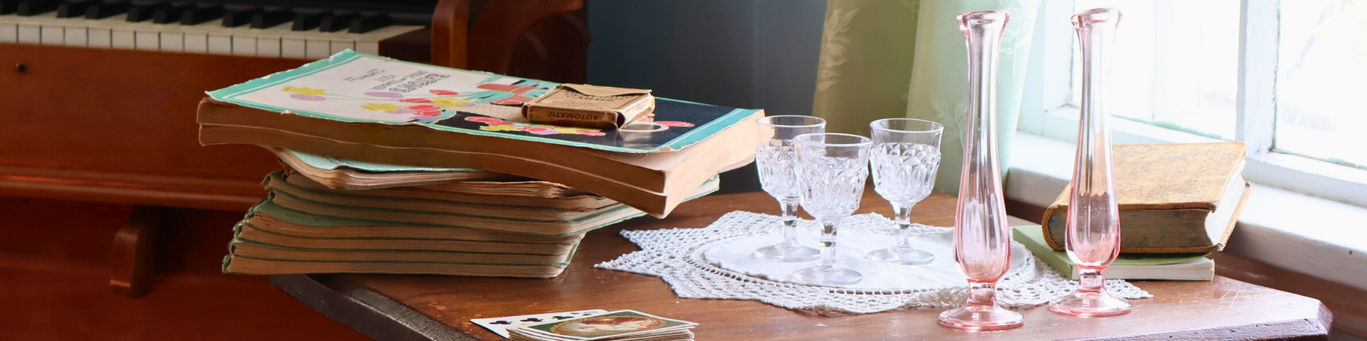 Miscellaneous objects on an antique coffee table: candleholders, glasses, books, magazines, playing cards. 