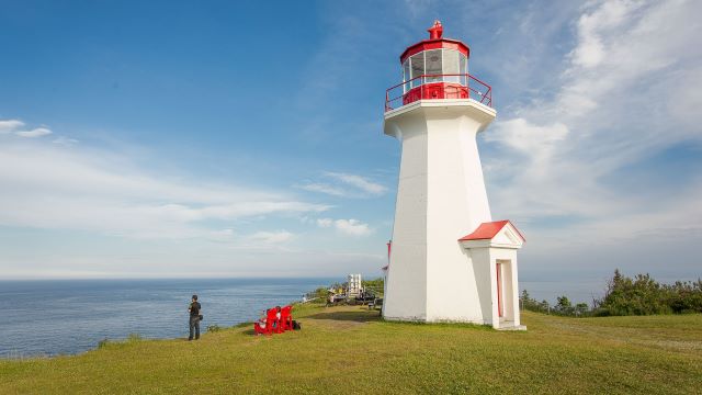 Visitors next to a lighthouse at the top of a cliff.