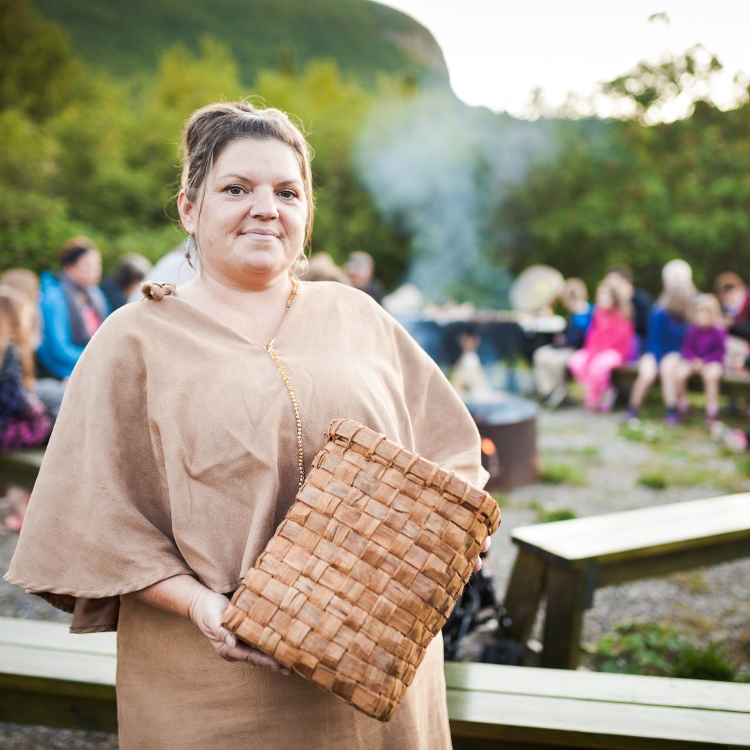 A woman in traditional Micmac dress holds a piece of basketry.