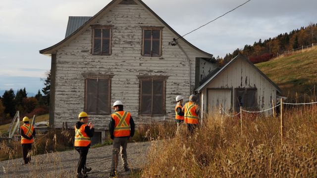 Five people in helmets and bibs look at a heritage house at a construction site.