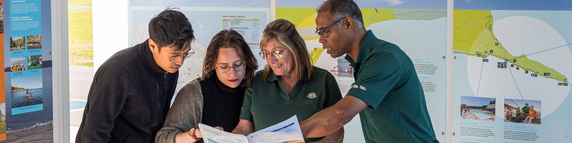 Two Parks Canada employees help two visitors with a brochure. 