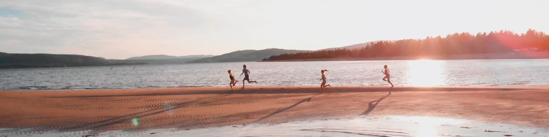 Children are running on a sand spit at sunset.