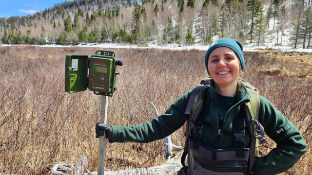 A Parks Canada employee holding a recording device near a pond in spring.