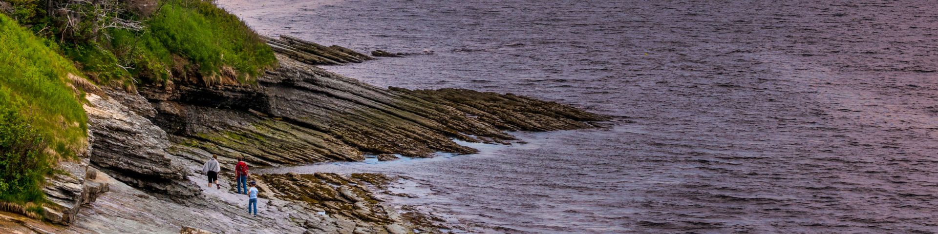 Trois personnes marchent sur le littoral vers des roches sédimentaires. 