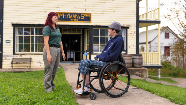 Une employée et un homme en fauteuil roulant échangent devant un ancien magasin général. 