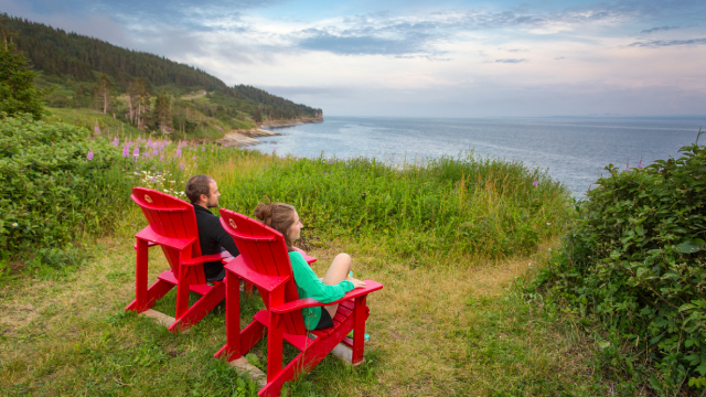 Deux personnes assises sur leur chaise rouge regardent sur une falaise la mer. 