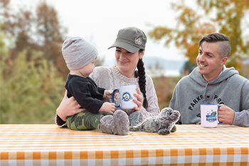 
A family of a man, a woman and a baby sit together holding two Forillon National Park mugs