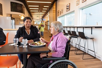 Two women, one in a wheelchair, share a meal at a restaurant in Forillon.