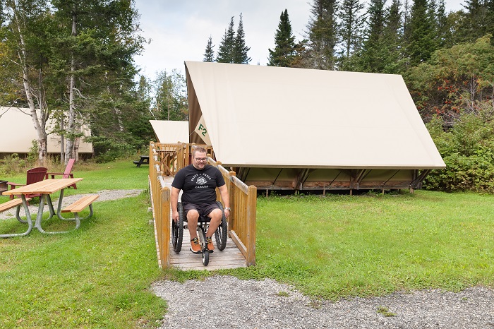 Un homme en fauteuil roulant descend la rampe d'accès qui mène à l'intérieur de la tente oTENTik F2 au camping Petit-Gaspé