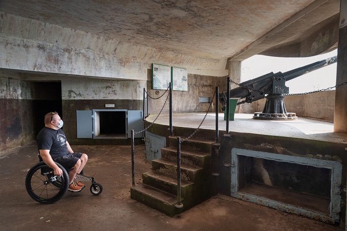 Un homme en fauteuil roulant admire un authentique canon à l'intérieur de la batterie côtière de Fort-Péninsule.