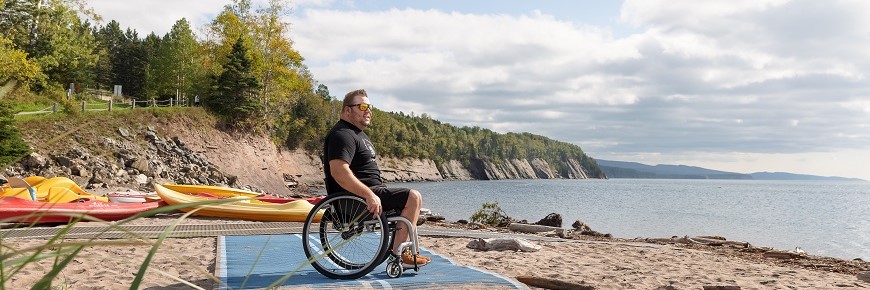 A man in a wheelchair is stopped on Penouille Beach’s universal mat and observes the sea.
