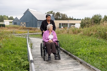 A woman in a wheelchair and a friend on a raised wooden walkway